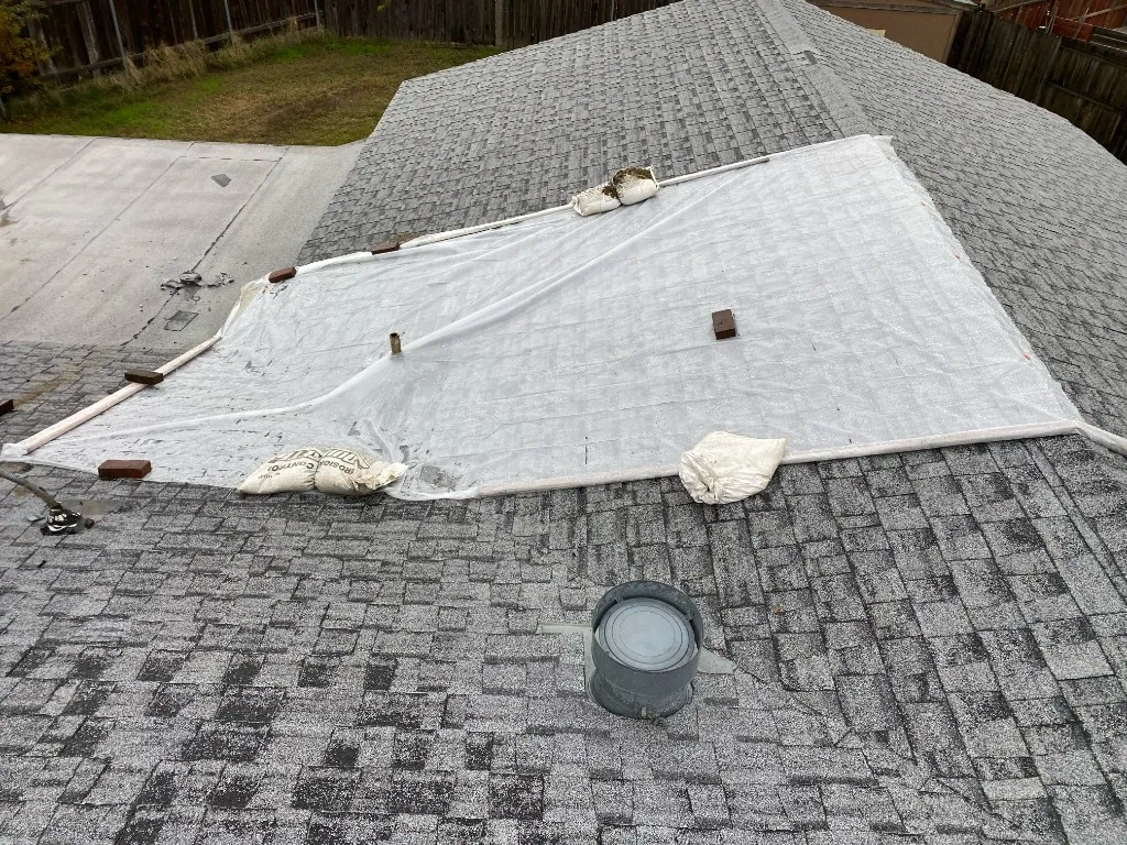 Large protective tarp secured over an exposed section of an asphalt roof